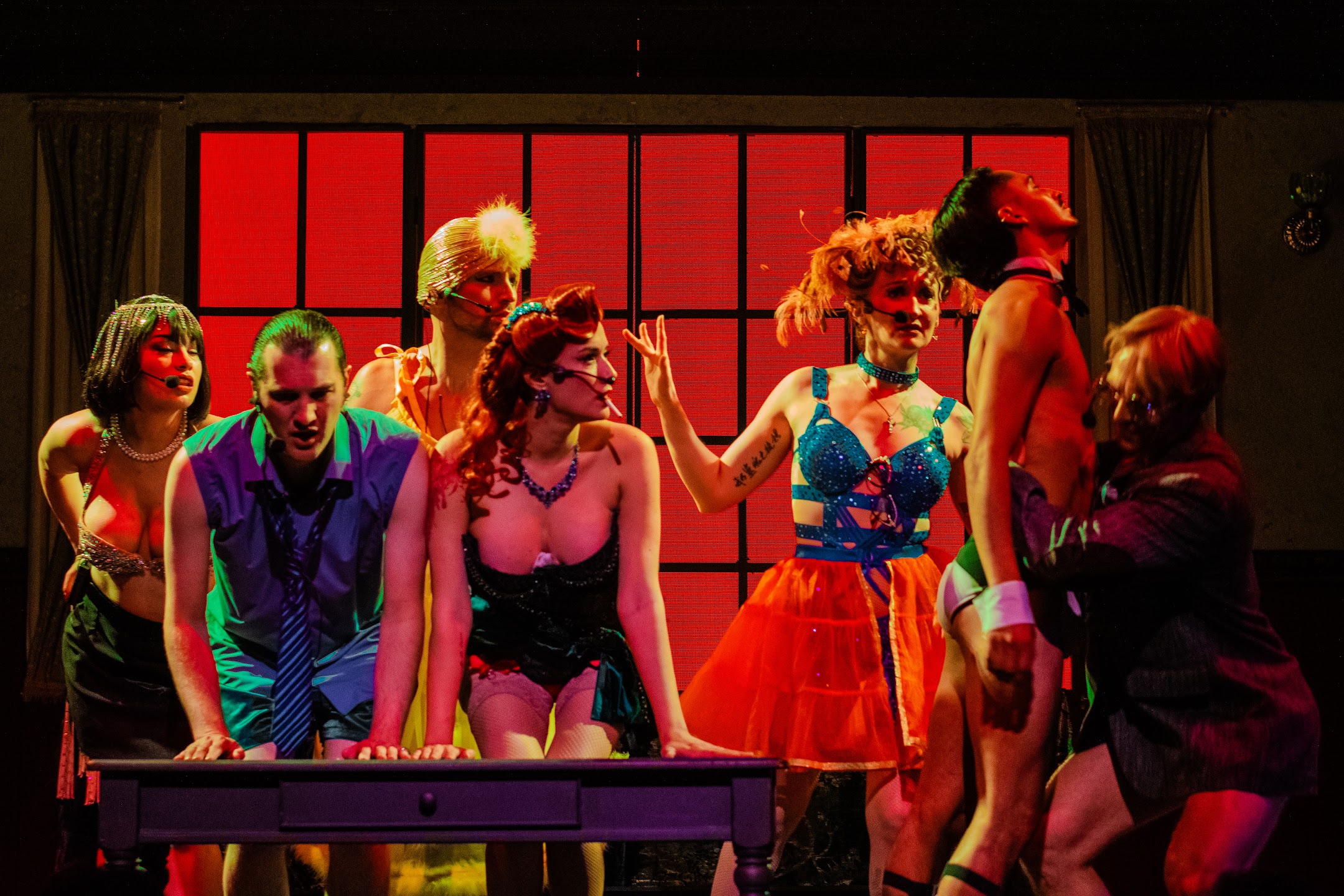 ClueX ensemble in colorful costumes around a desk onstage